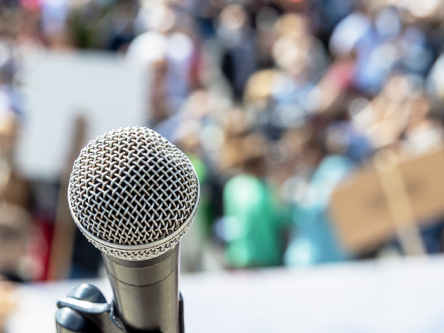 An image of a microphone with a an audience blurred in the background